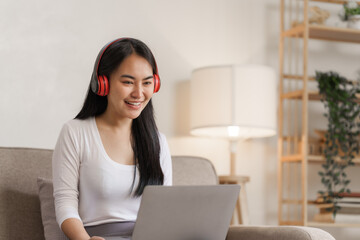 Smiling young asian woman enjoying free time while relaxing with her laptop in living room..