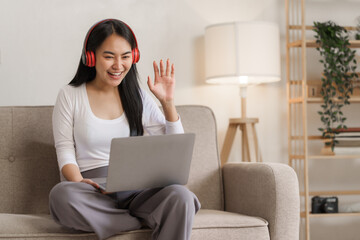 Fototapeta premium Young happy asian woman using laptop and headphones online meeting with friends via online conference remote meeting.