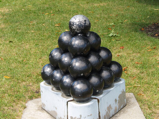 Stack Of Black Round Cannon Balls On Cement Platform Green Grass