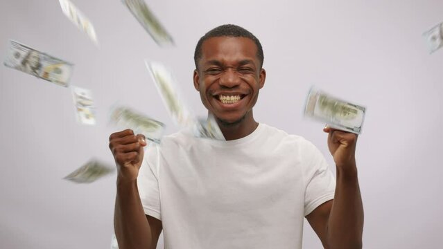 Happy african american man stands in the rain of dollars on white background.