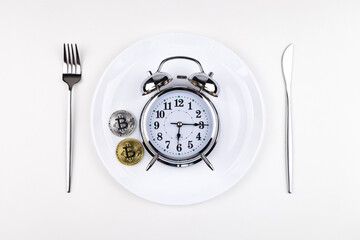 Top view alarm clock on a white plate with a knife and fork on a white background. Intermittent...
