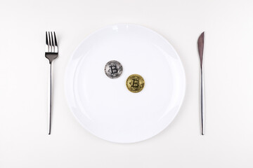 bitcoins on a white plate with cutlery on a white table. View from above