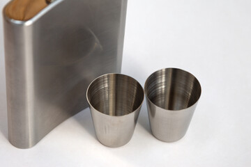 A metal flask for drinks and metal cups next to each other on a white background. For storing...