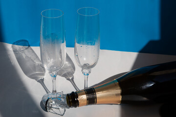 Two misted champagne glasses and an empty champagne bottle close-up on a blue and white background. After the holiday, the end of a romantic evening. End of the party