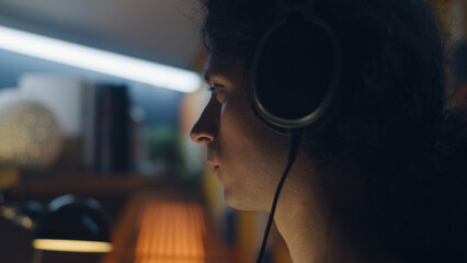 Man in headphones browsing the internet and social networks on computer at home at night and listening to music or having online freelance work