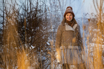 sweet girl in woollen hat, jumper, black skirt and tights enjoys the freezing cold winter and plays with snow