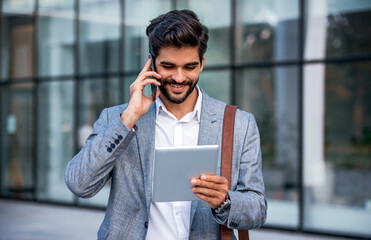 Businessman holding tablet and making a phone call in front of the corporation. Business, lifestyle concept