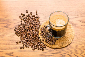 cup of coffee fresh brew on rustic wood grain table with coffee beans. Traditional morning hot cup of coffee with crema. High angle view of table top