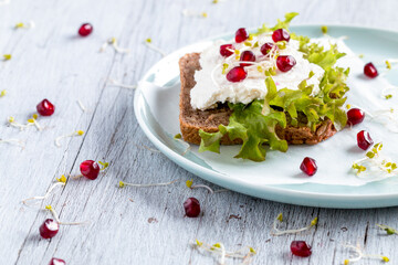 Dark bread sandwich with grains. Top with green lettuce, cottage cheese, pomegranate, and sprouts. Everything on a rustic wooden table. - 533050044