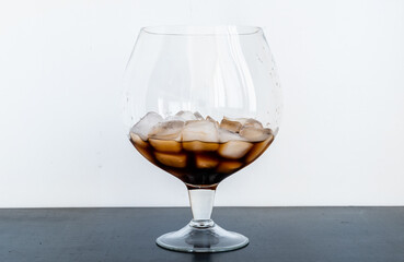 Dark drink with ice in transparent glassful on black table on white background
