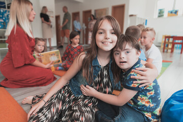 A girl and a boy with Down's syndrome in each other's arms spend time together in a preschool...
