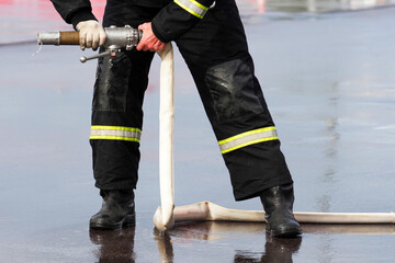 Firefighter holding a fire hose with water in his hands, extinguishing a fire