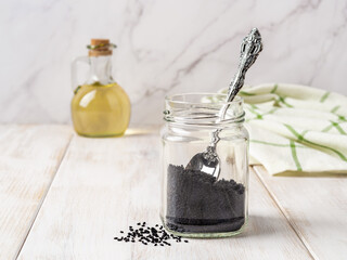 Dry nigella seeds and spoon in a glass jar on a white wooden countertop. Using black cumin for...