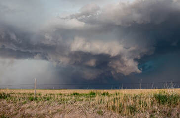 A severe thunderstorm darkens the sky with ominous clouds over farmland in the great plains.
