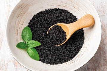 Black cumin seeds and wooden spoon in a white bowl. Using kalonji dry seeds for cooking. Concept of...