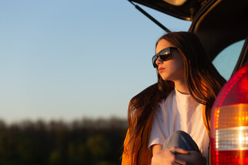 Pretty sad teenage girl with sun glasses sitting alone in a car trunk.