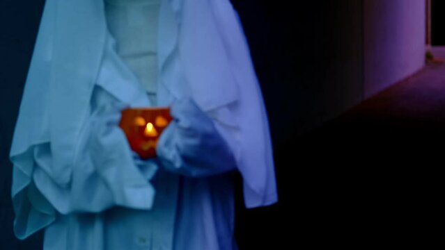 ghost boy in white hoodie holds pumpkin candle in her hands in creepy tunnel, sad child ghost at night, halloween festival concept, frightening mystical events, friday the 13th, horror movie scene