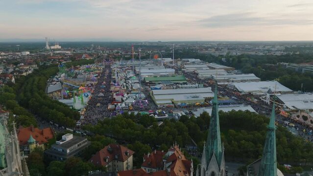 Crowd of Oktoberfest visitors at dusk. Famous beer and folk festival. Backwards reveal of towers of St. Pauls Church. Munich, Germany
