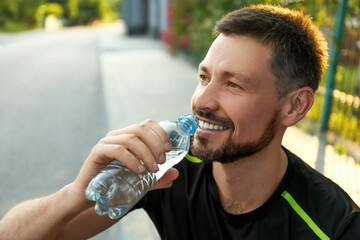 Happy man drinking water outdoors on hot summer day. Refreshing drink