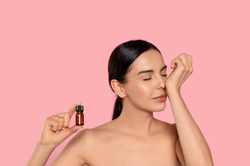 Young woman smelling essential oil on wrist against pink background
