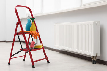 Ladder with cleaning supplies near modern radiator in room