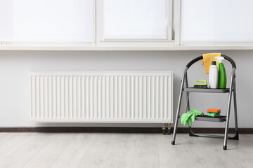 Ladder with cleaning supplies near modern radiator in room