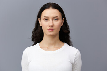 a gentle woman stands on a dark background in a tight white T-shirt, calmly lowered her hands down and looks forward