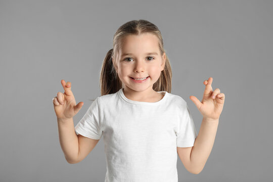 Child with crossed fingers on light grey background. Superstition concept