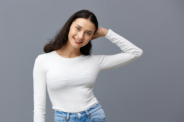 an attractive woman stands on a gray background in a white T-shirt, hid her hands behind her back,...