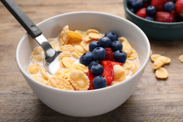 Bowl of tasty crispy corn flakes with milk and berries on wooden table, closeup