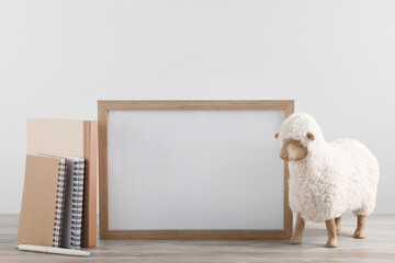 Blank photo frame, notebooks and decorative sheep on wooden table