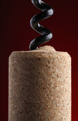 Corkscrew with cork against dark red background, closeup