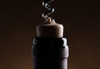 Opening wine bottle with corkscrew on dark brown background, closeup