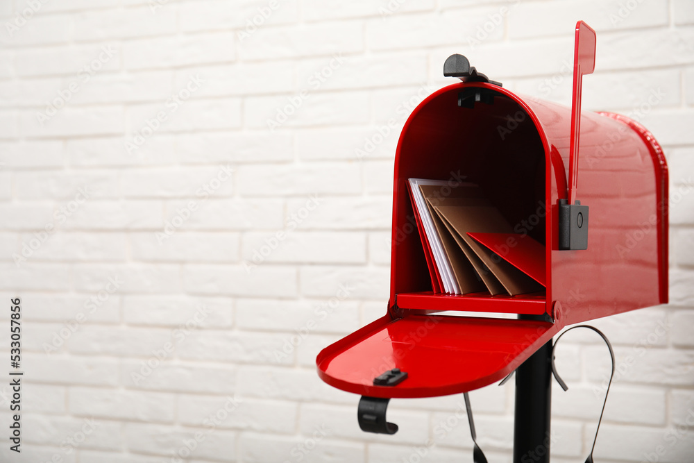 Wall mural Open red letter box with envelopes near white brick wall. Space for text