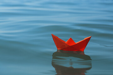 Orange paper boat floating on water surface, space for text