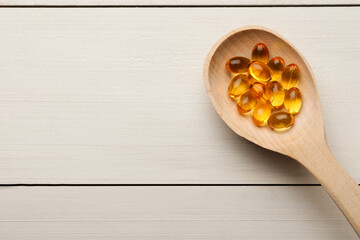 Spoon with dietary supplement capsules on white wooden table, top view. Space for text