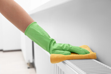 Woman cleaning radiator with rag indoors, closeup