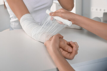 Doctor applying bandage onto patient's arm in hospital, closeup