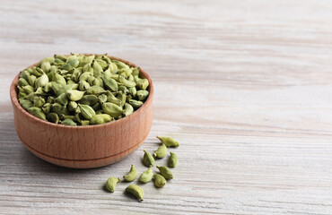 Bowl with dry cardamom pods on wooden table. Space for text