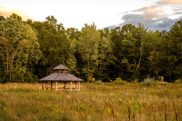New Paltz, NY - USA - Sept. 22, 2022 Horizontal sunset view of the scenic Testimonial Gateway Trail's iconic wooden gazebo, situated off the path in a grassy field, with a thick tree line behind it.