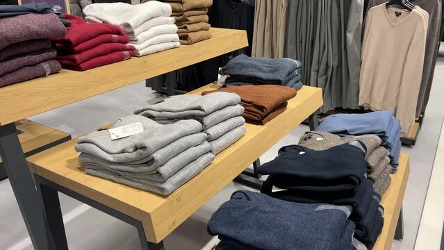 Stacks of textile pullovers lie on the shelves of a clothing store