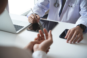 Doctor and patient talking at medical examination at hospital office, close-up. Doctor using digital tablet filling up electronic health records and prescription. Medicine and healthcare concept