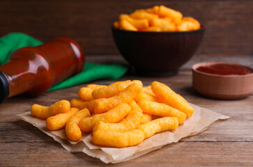 Crunchy cheesy corn snack and ketchup on wooden table, closeup