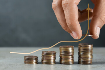 Salary increase concept. Woman stacking coins on grey table and illustration of up arrow