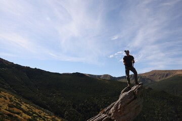 Man with backpack and trekking poles on rocky peak in mountains