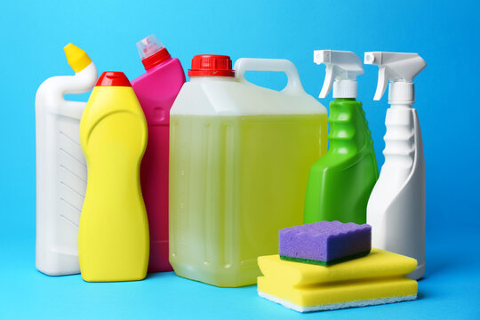 Bottles of detergents and sponges on light blue background. Cleaning supplies