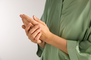 Woman applying cosmetic cream onto hand on light grey background, closeup