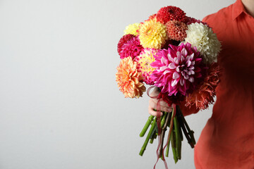 Woman with bouquet of beautiful dahlia flowers on light background, closeup. Space for text
