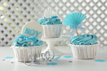 Delicious cupcakes with light blue cream and toppers for baby shower on white table