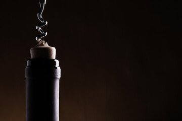 Opening wine bottle with corkscrew on dark background, closeup. Space for text